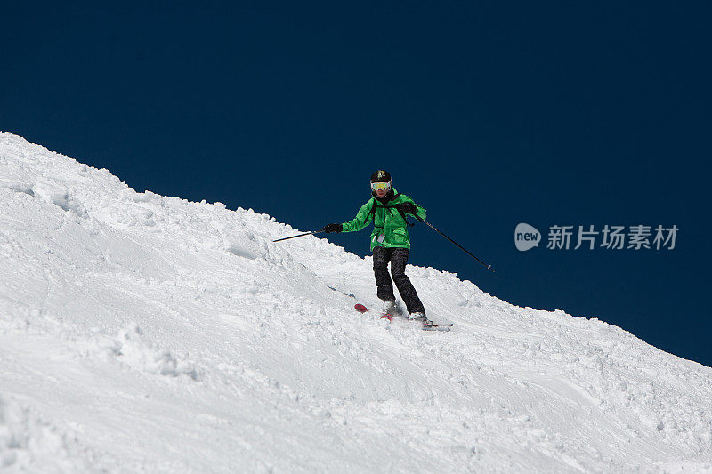 专业成熟的女性滑雪者在一个非常陡峭的斜坡上，对着明亮的蓝色天际线。