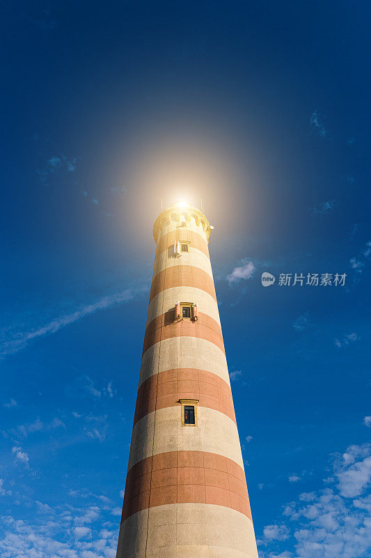古老的条纹灯塔灯塔，明亮明亮的蓝色天空闪闪发光。灯塔的主要用途是作为辅助航行的灯塔。垂直的旗帜。想法的概念