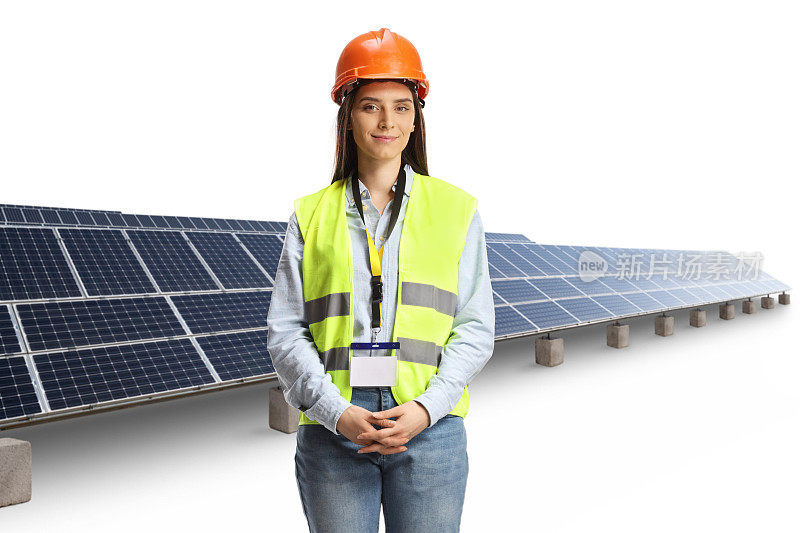 年轻的女工程师，穿着安全背心，戴着安全帽，站在太阳能电池板前