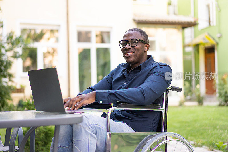 一位坐在轮椅上的快乐男子正在花园里用笔记本电脑工作