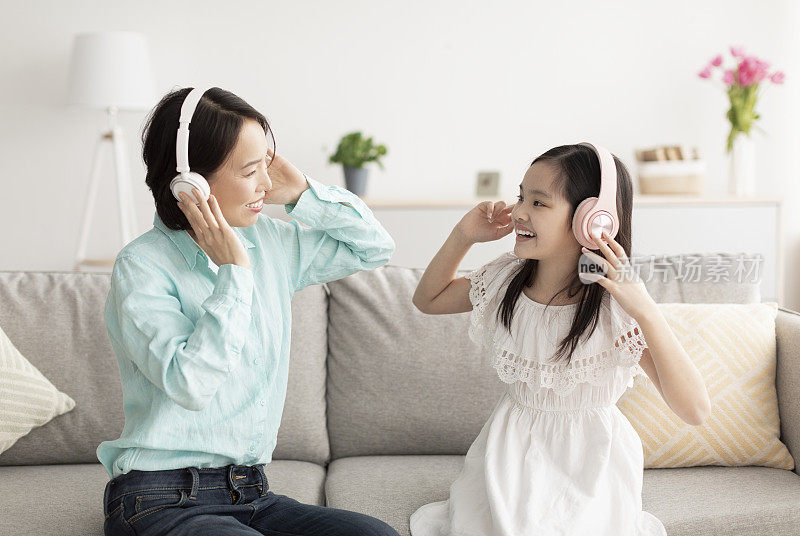 可爱的亚洲小女孩和她的祖母戴着耳机一起坐在家里的沙发上听音乐