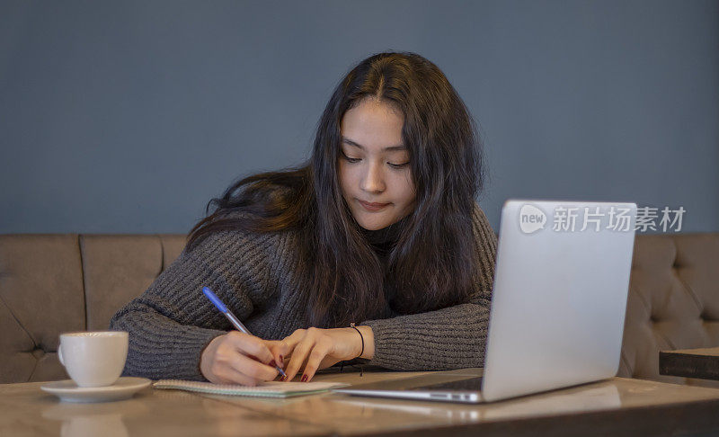 一名年轻的亚洲女子在咖啡馆边喝咖啡边摆弄电脑