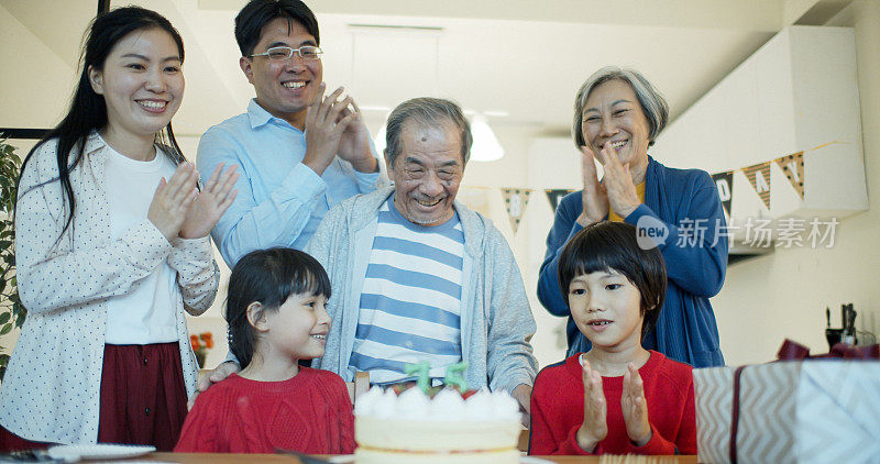 亚洲祖父在家人的簇拥下吹灭生日蛋糕蜡烛