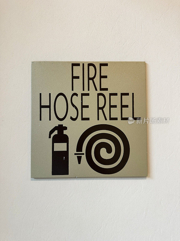 现代壁挂式消防水管卷筒标志的特写图像，黑色灭火器和软管卷筒符号固定在墙上的方形黄铜牌匾上，消防安全概念