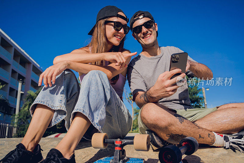 一对快乐的年轻情侣拿着滑板在滑板公园自拍