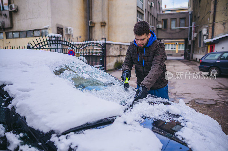 年轻人正在清除汽车上的积雪