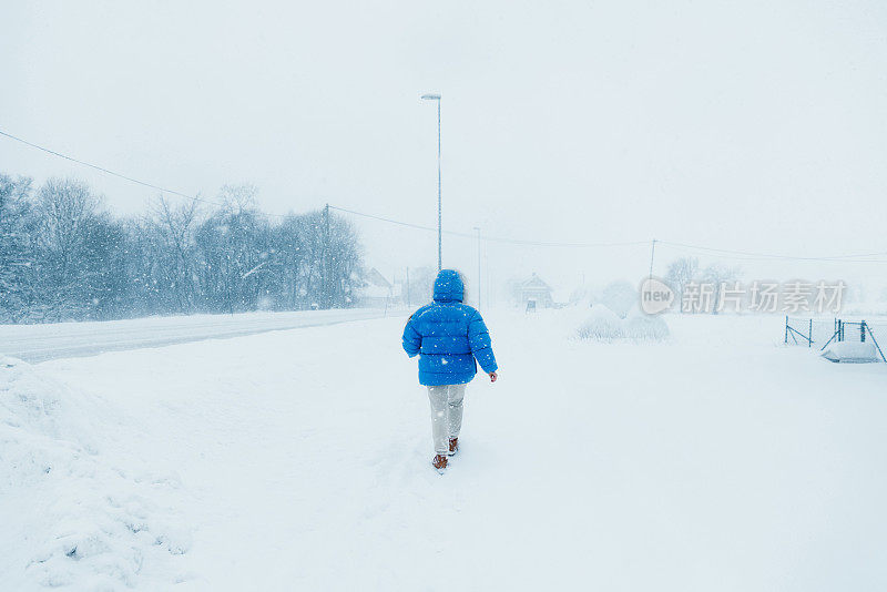 一名穿着蓝色外套的女子在大雪中漫步在斯堪的纳维亚村庄的街道上，欣赏冬天