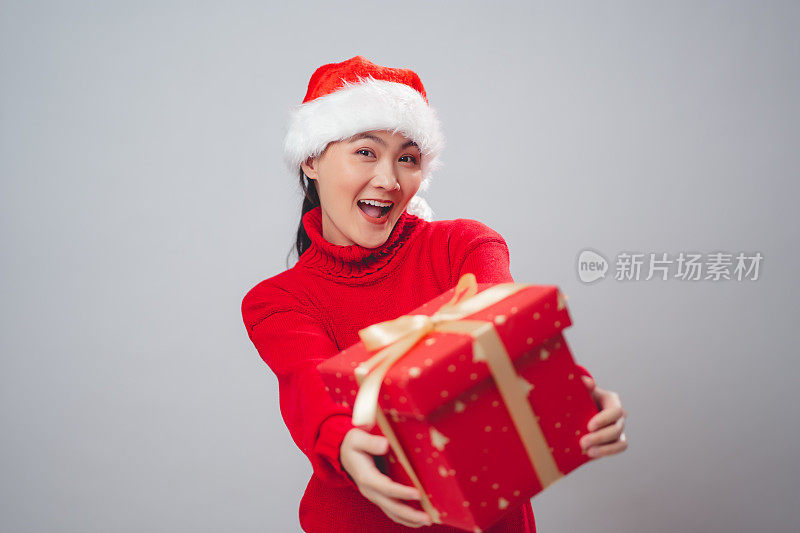 亚洲妇女戴着圣诞老人帽，开心地微笑着展示礼盒，孤立在白色背景上。
