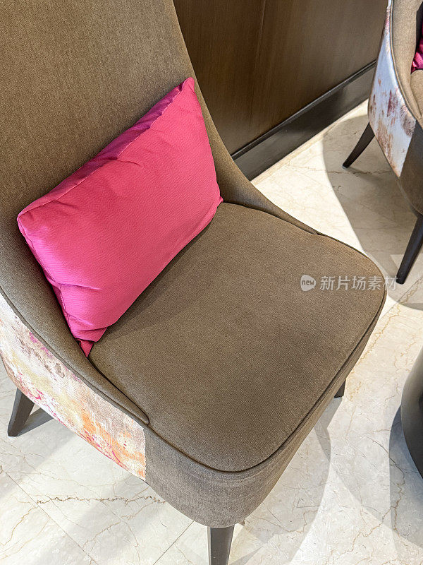 棕色材料覆盖的高靠背椅子与明亮的粉红色靠垫的特写图像，瓷砖地板，木板墙背景，抬高的观点