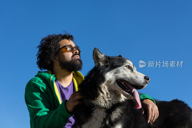 墨西哥城，一只哈士奇狗伸出舌头，旁边是它的主人，背景是天空
