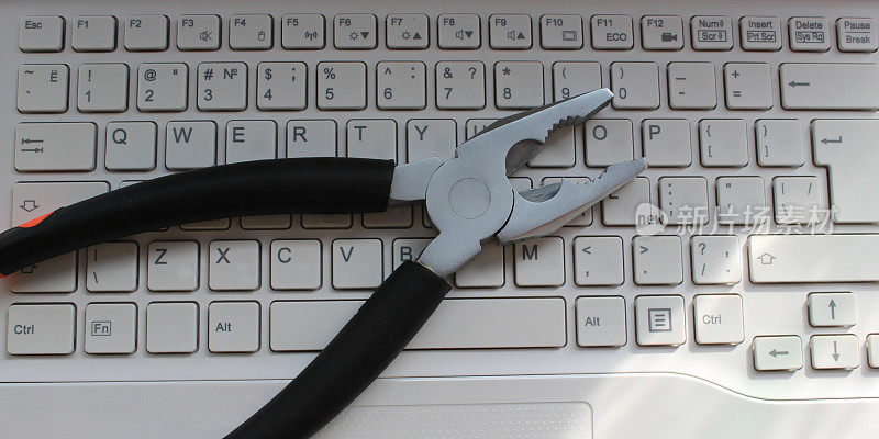 钳子放在白色的电脑键盘上，键盘上只有拉丁字符