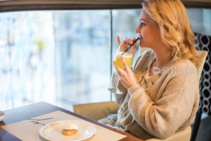 微笑的女人享受在一杯橙汁在咖啡馆。