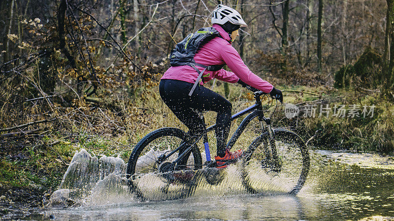 女性山地自行车骑过小溪水在森林