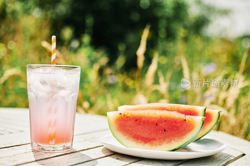 在一个炎热的夏天，花园的桌子上放着几片西瓜和一杯冰柠檬水。