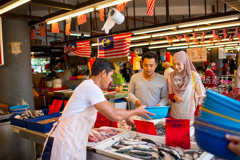 一对亚洲马来夫妇在菜市场的鱼摊上买海鲜