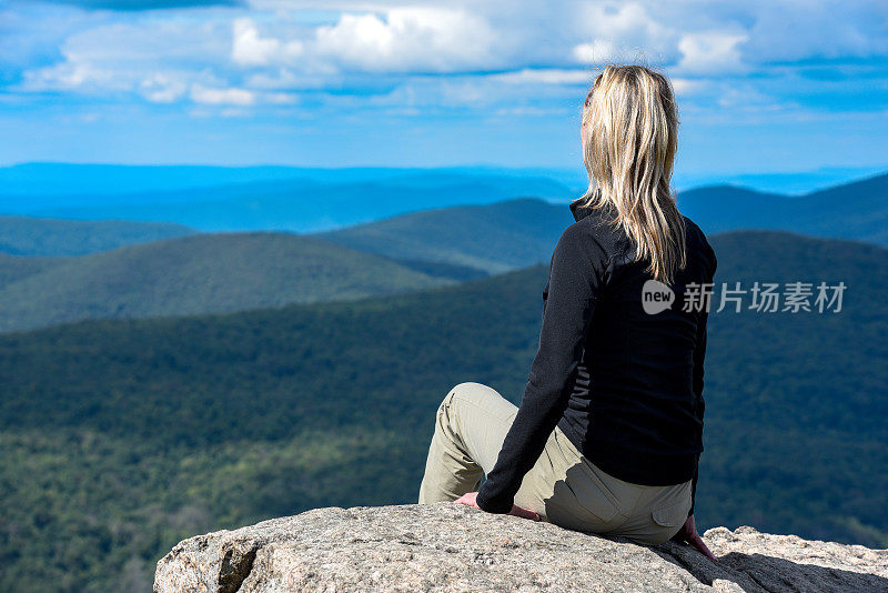 年轻的女子站在山顶，望着地平线