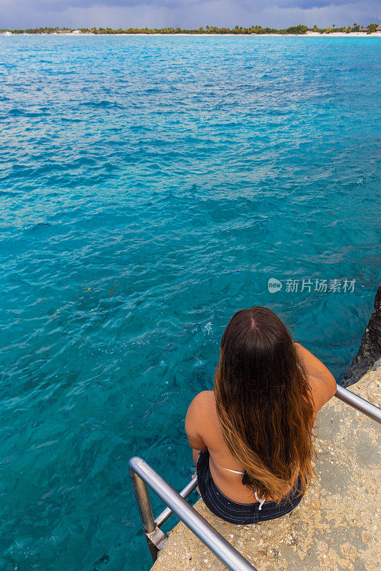 年轻女子坐在前面的水大海-凝视着大海