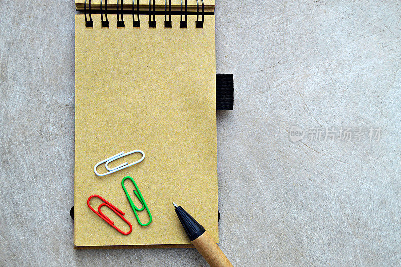 米色素色页螺旋装订记事本与一支钢笔和彩色回形针