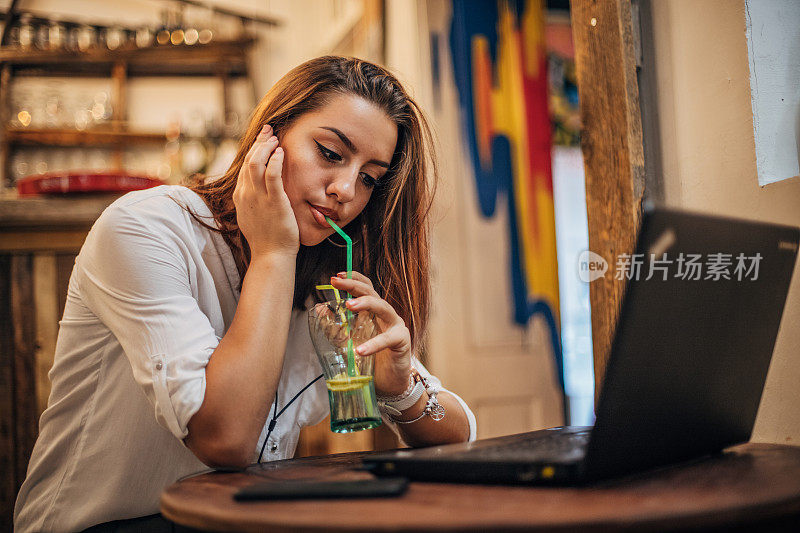 一个年轻漂亮的女人喝着苏打水，用着笔记本电脑