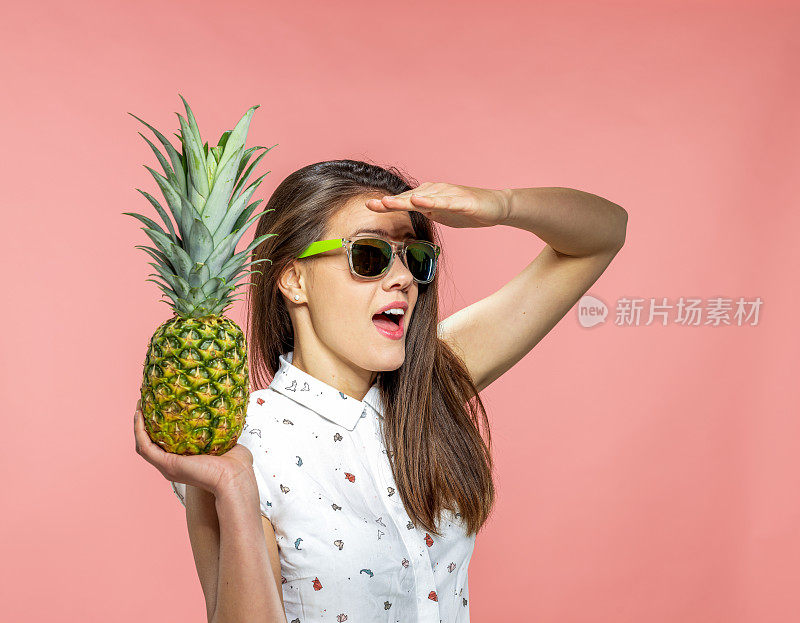 年轻女子戴着墨镜，拿着菠萝在珊瑚的背景和看别处
