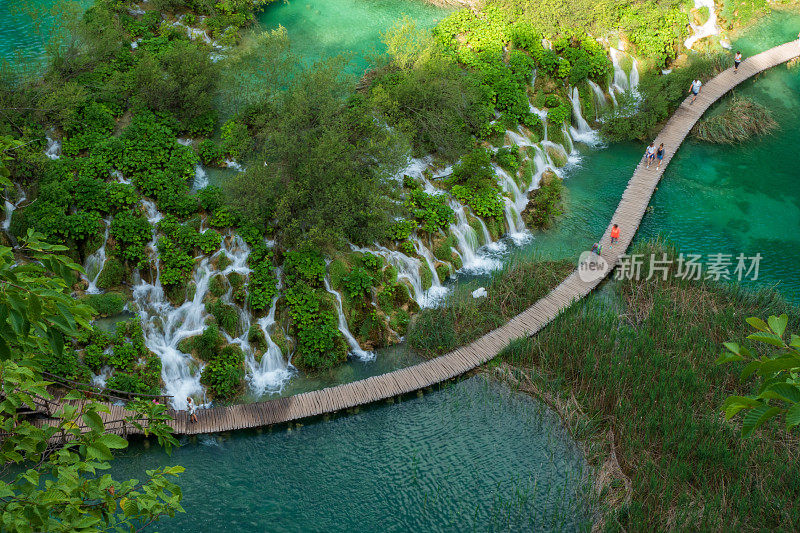 在克罗地亚的普利特维茨湖国家公园，徒步旅行者经过瀑布，水流冲下进入绿松石色的湖泊Kaluđerovac