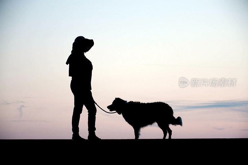 成熟的西班牙妇女和牧羊犬剪影日落