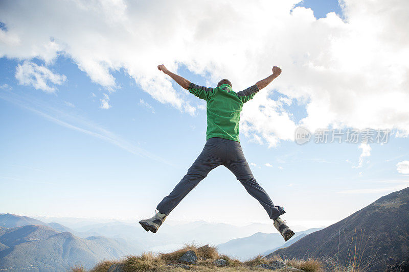 年轻的徒步旅行者在山顶上为成功而跳跃