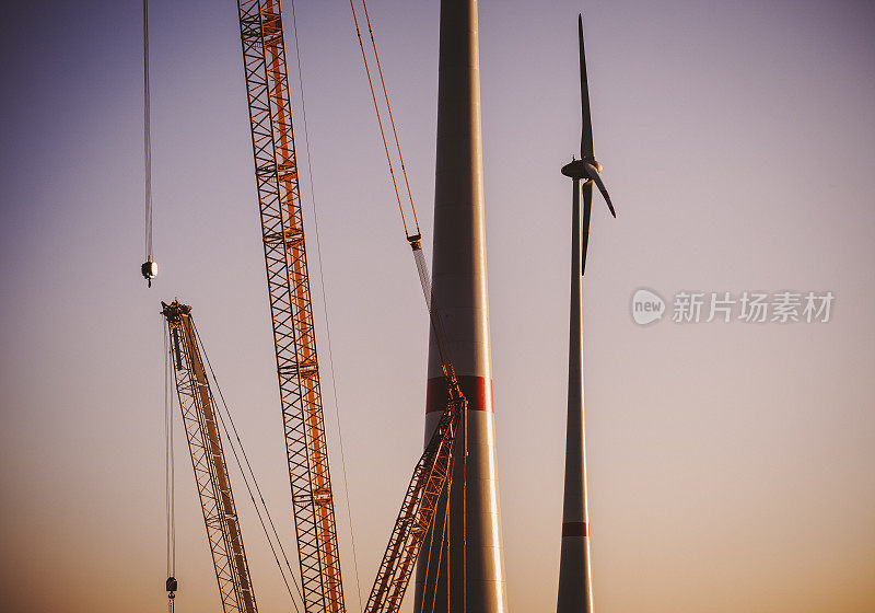 日落时分，两台风力涡轮机和一台建筑起重机