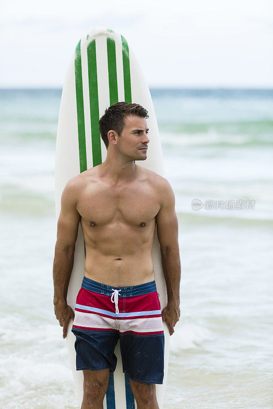 赤裸上身的年轻人站在海滩冲浪板前