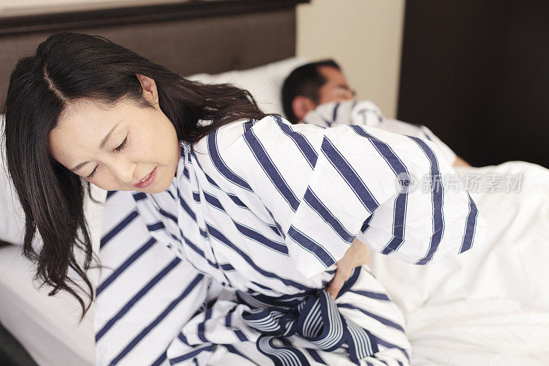 坐在床上遭受背痛的日本妇女
