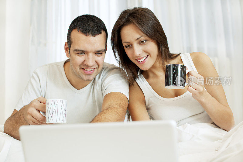 在床上喝咖啡，用笔记本电脑工作的夫妇