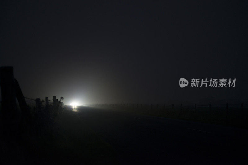 夜晚，在大雾弥漫的乡间小路上，一辆驶近的汽车
