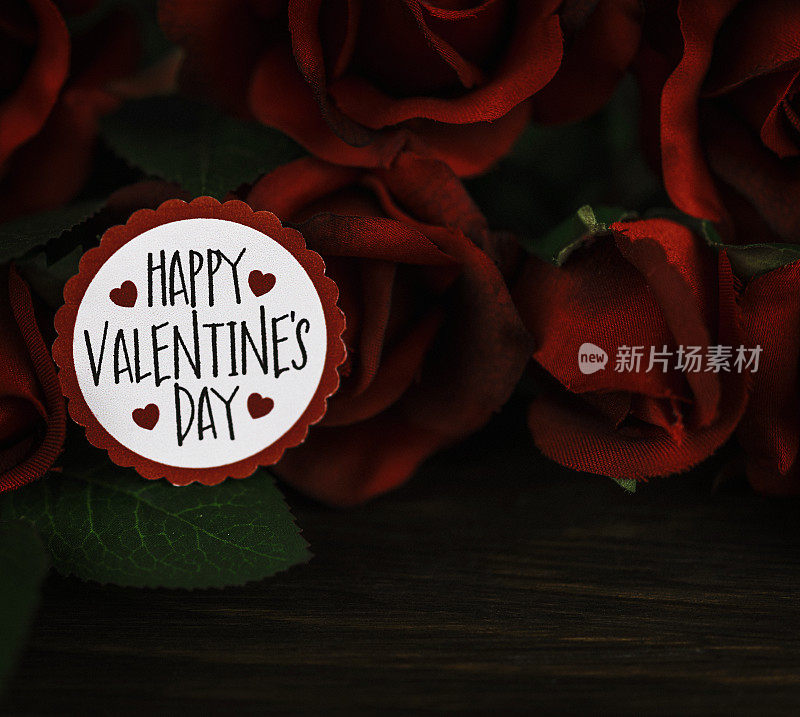 情人节的红玫瑰花束放在质朴的木桌上，上面有留言