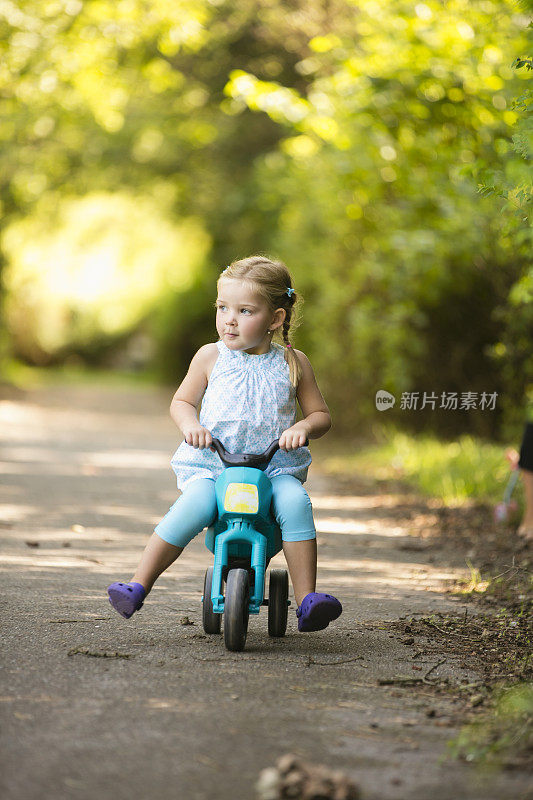 小女孩坐在公园里的玩具摩托车上