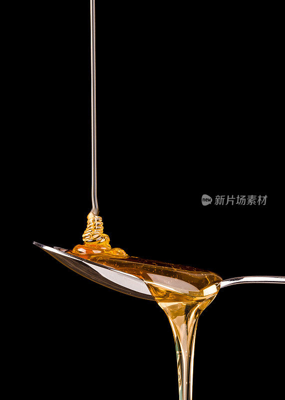 金色的蜂蜜，银色的勺子，黑色的背景