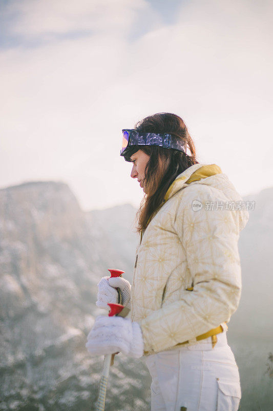 近景美丽的年轻女子在冬天的衣服站在一边，手拿木棍的背景雪山