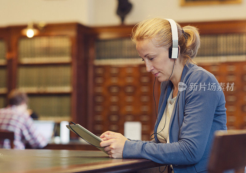 图书馆里戴着耳机使用平板电脑的成熟女性。