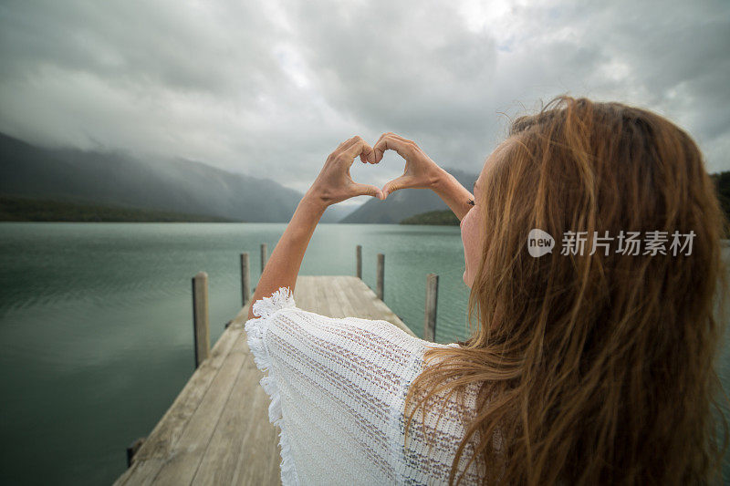 湖边码头上的年轻女子做了心形的指架