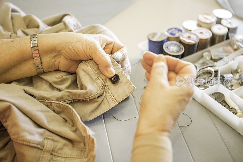 系列:老妇人的手在缝裤子上的纽扣