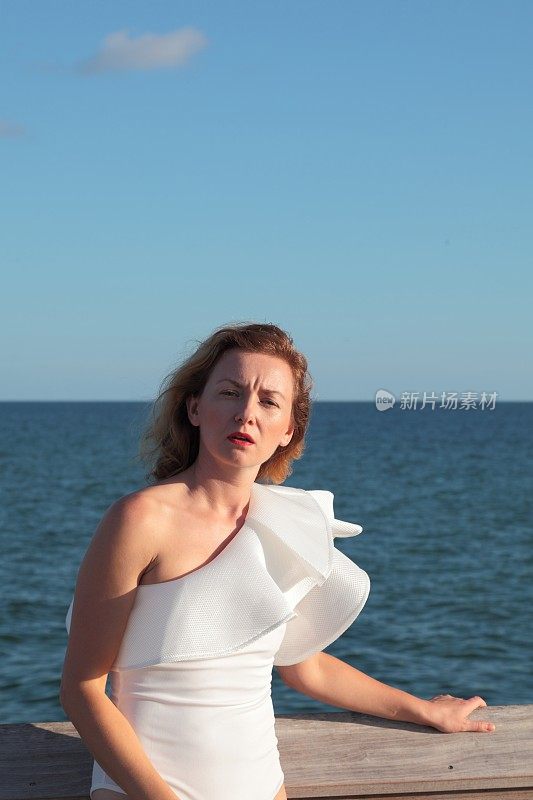 年轻女子站在一件白色泳衣前的大海。