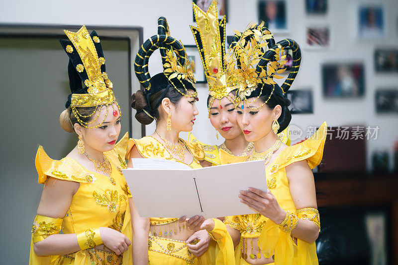 四位亚洲女演员穿着泰国传统的黄色服装读着空白的课本