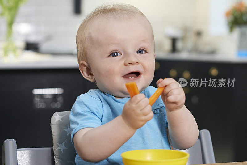 快乐的幼童坐在桌前吃新鲜的胡萝卜