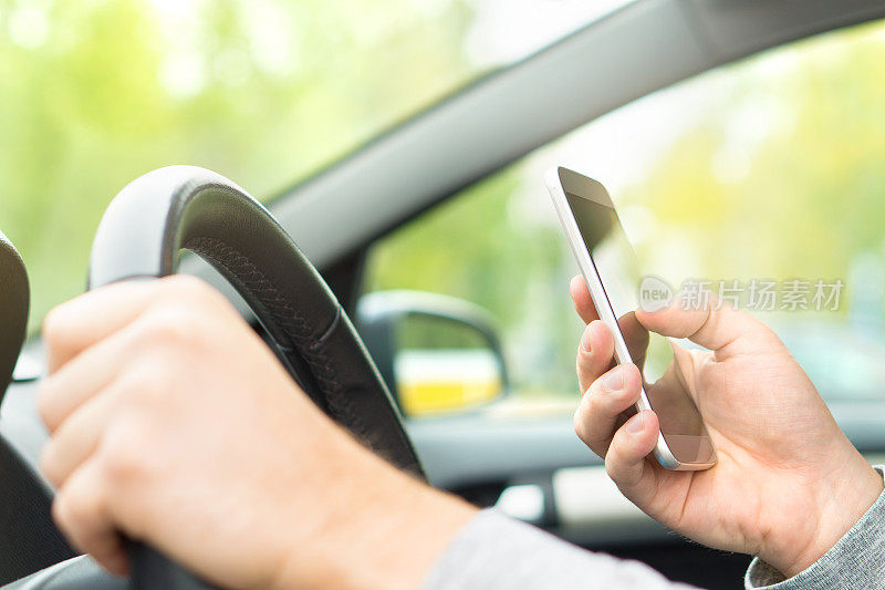开车时使用智能手机的男人。司机在车里发短信和使用手机。在车上用手机写和打字信息。另一只手握住方向盘。