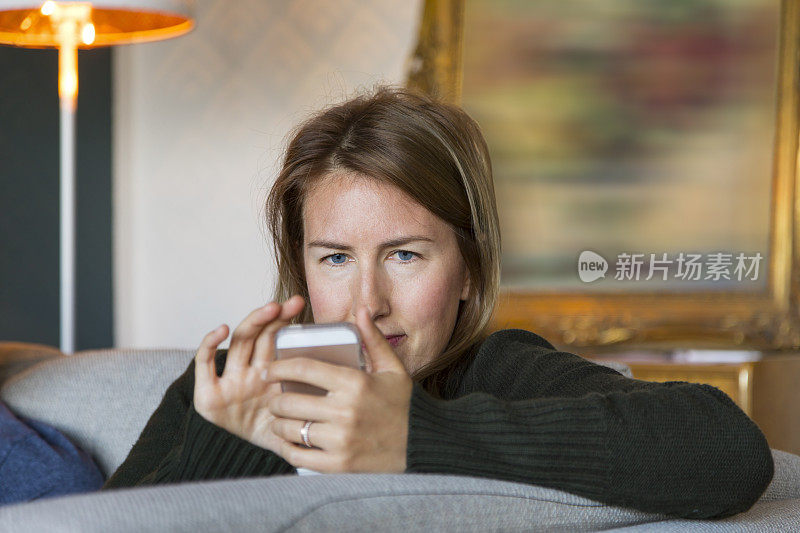 一名年轻女子在家中沙发上休息时使用智能手机