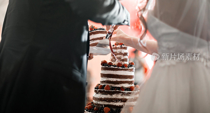 新娘和新郎切结婚蛋糕。圆形多层海绵，奶油，果酱和浆果在一个圆形的基础上。新鲜的蓝莓和草莓