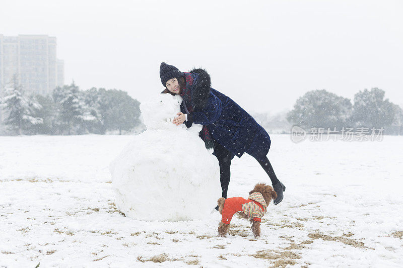 一个快乐的女人和她的狗在雪地上堆了一个大雪人