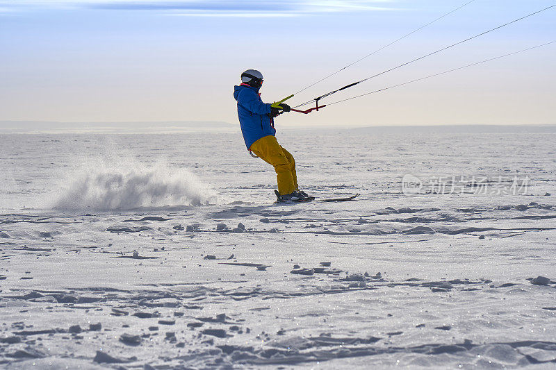 一个男运动员正在一个大的雪湖上的冰上放风筝。他在雪地里滑雪。冬天晴朗有霜的一天。