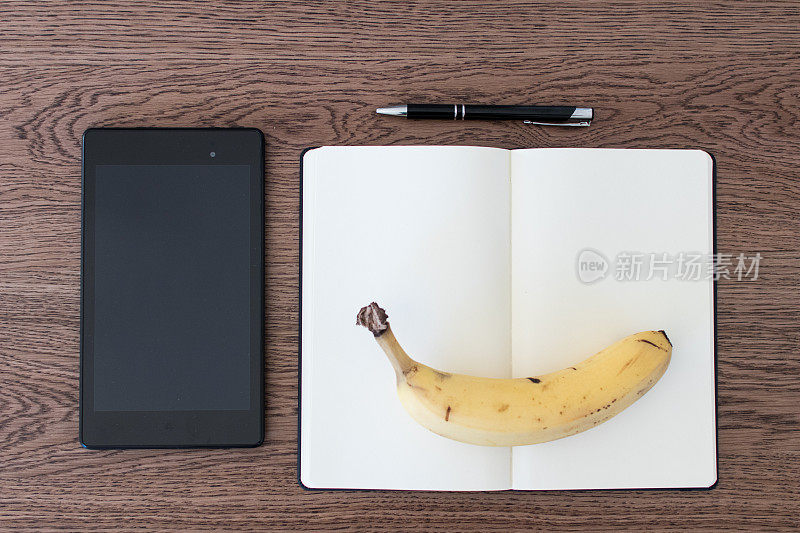 木桌上放着写字板、笔记本、笔和一根香蕉。假新闻的概念