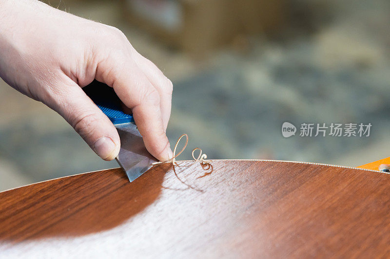 一个真实的男性木匠不精心打理的手的特写，通过切断剥离的装饰条的边缘来完成家具的刨花板细节。手工制作家具的概念源自