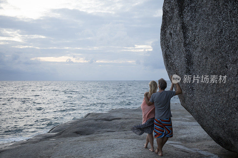 一对夫妇靠在海岸线上的巨石上